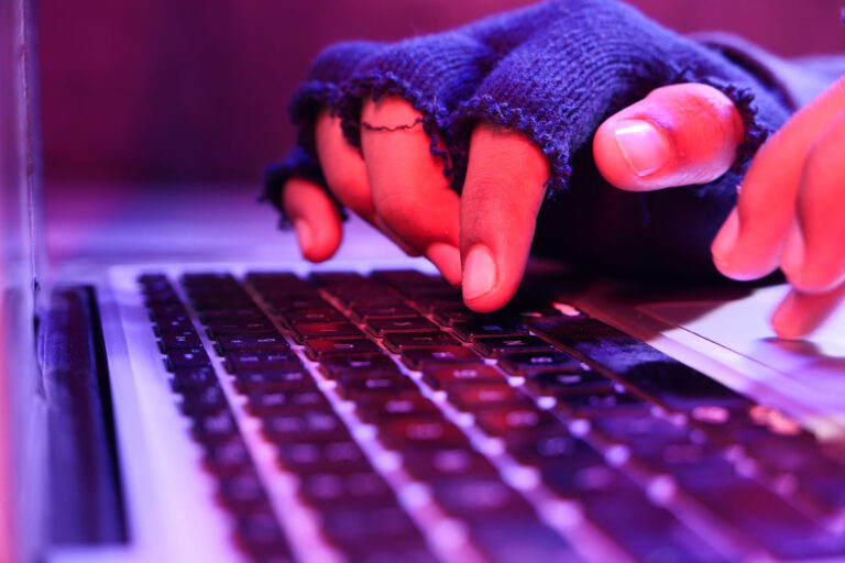 Hacker typing on a laptop with gloved hands in low light