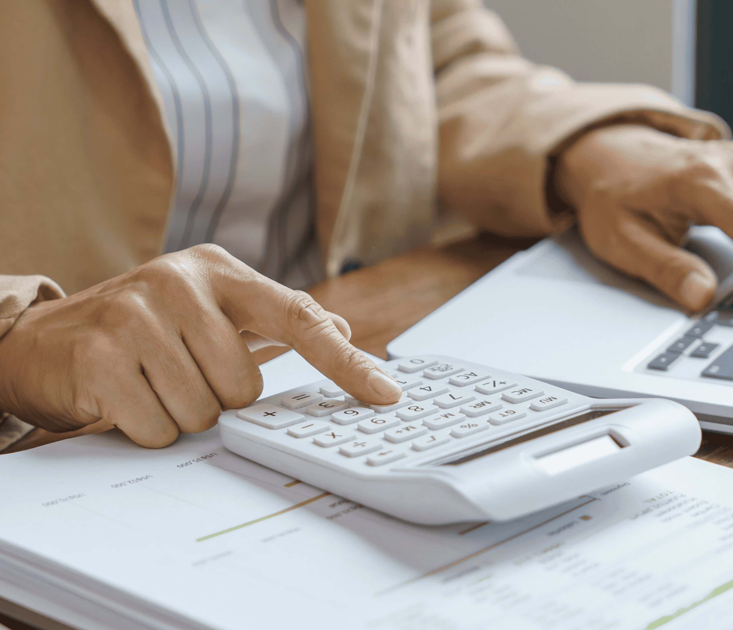 Close-up of hands pressing keys on a white calculator beside printed documents on a desk.