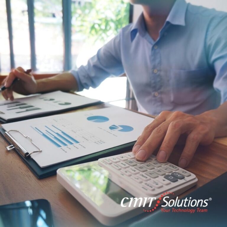 Financial professional reviewing charts and using a calculator, CMIT Solutions logo visible on desk