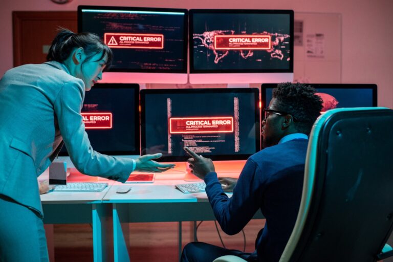 Two IT specialists discussing a critical error alert on multiple computer screens