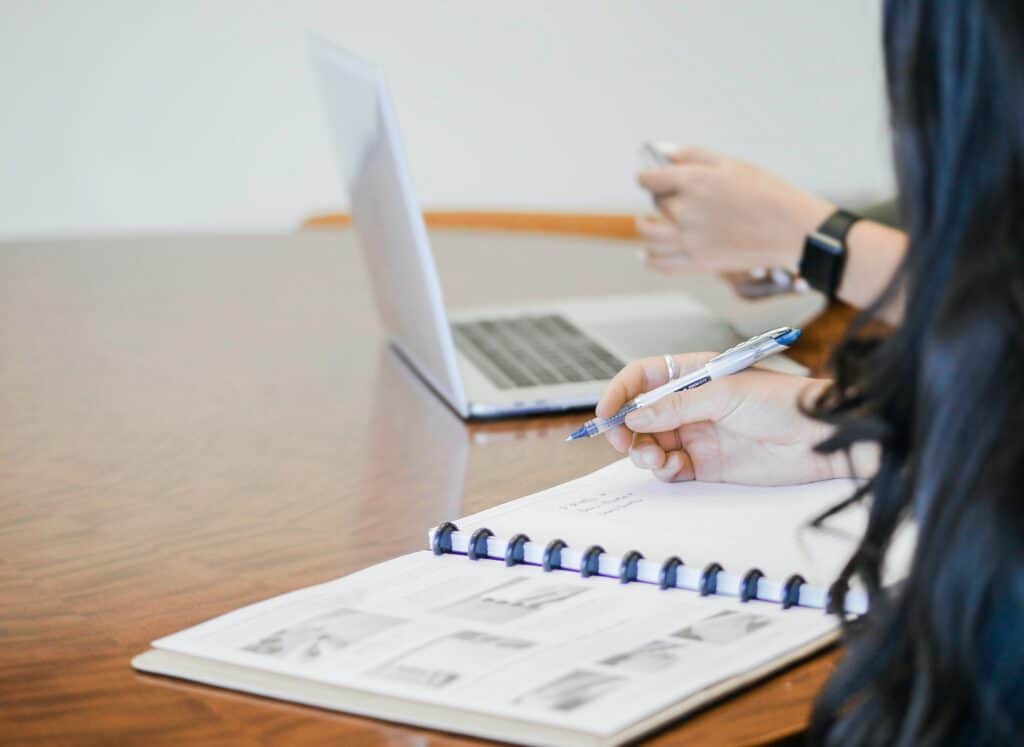 woman taking notes next to an open laptop