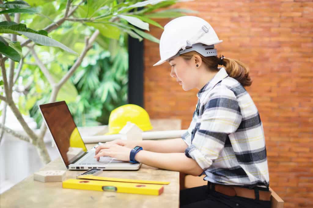 A female construction worker sits at a laptop outdoors 