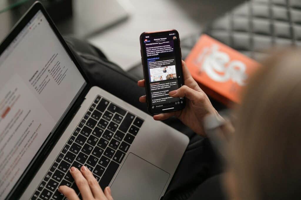 Person checking messages on a smartphone while working on a laptop