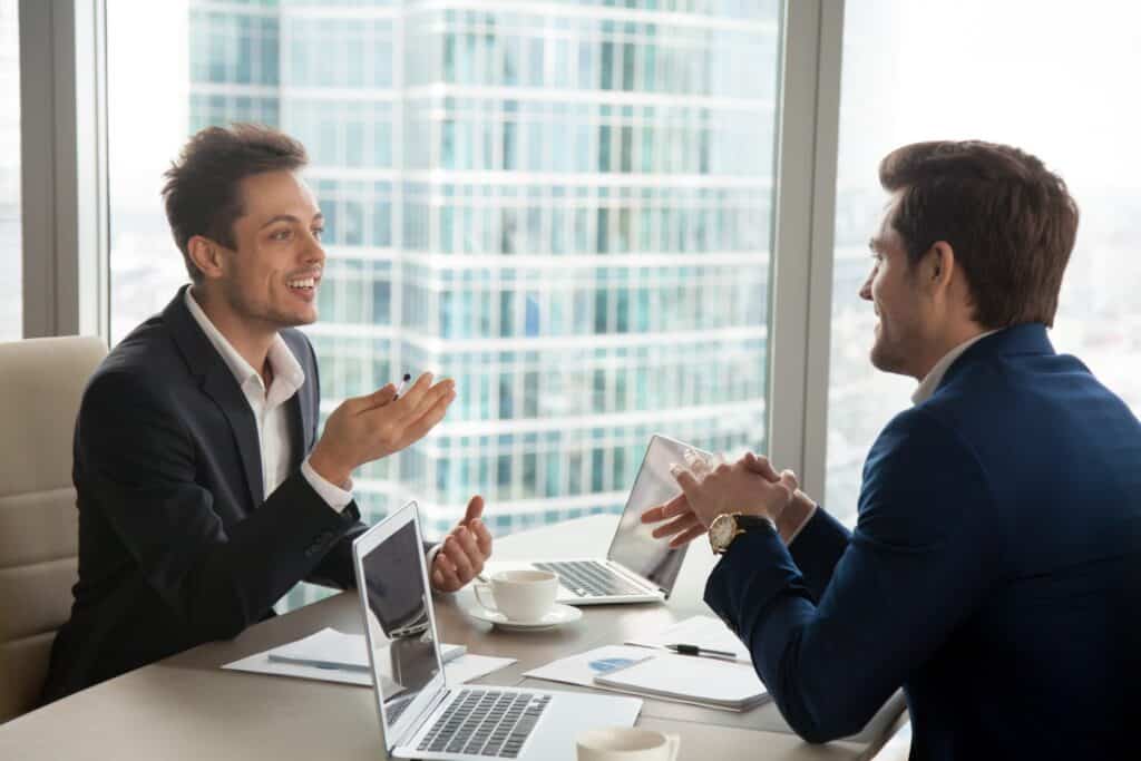 Two employees work on a project simultaneously on their laptops while discussing it candidly.