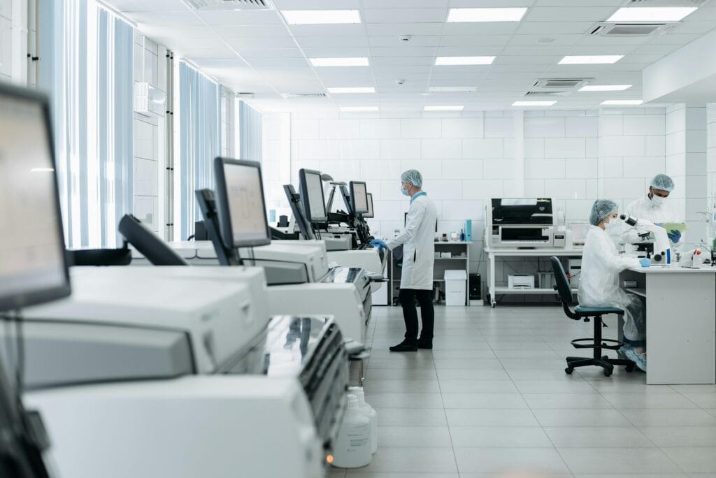 Healthcare workers standing at desks, looking at computer screens in a back room office/lab.