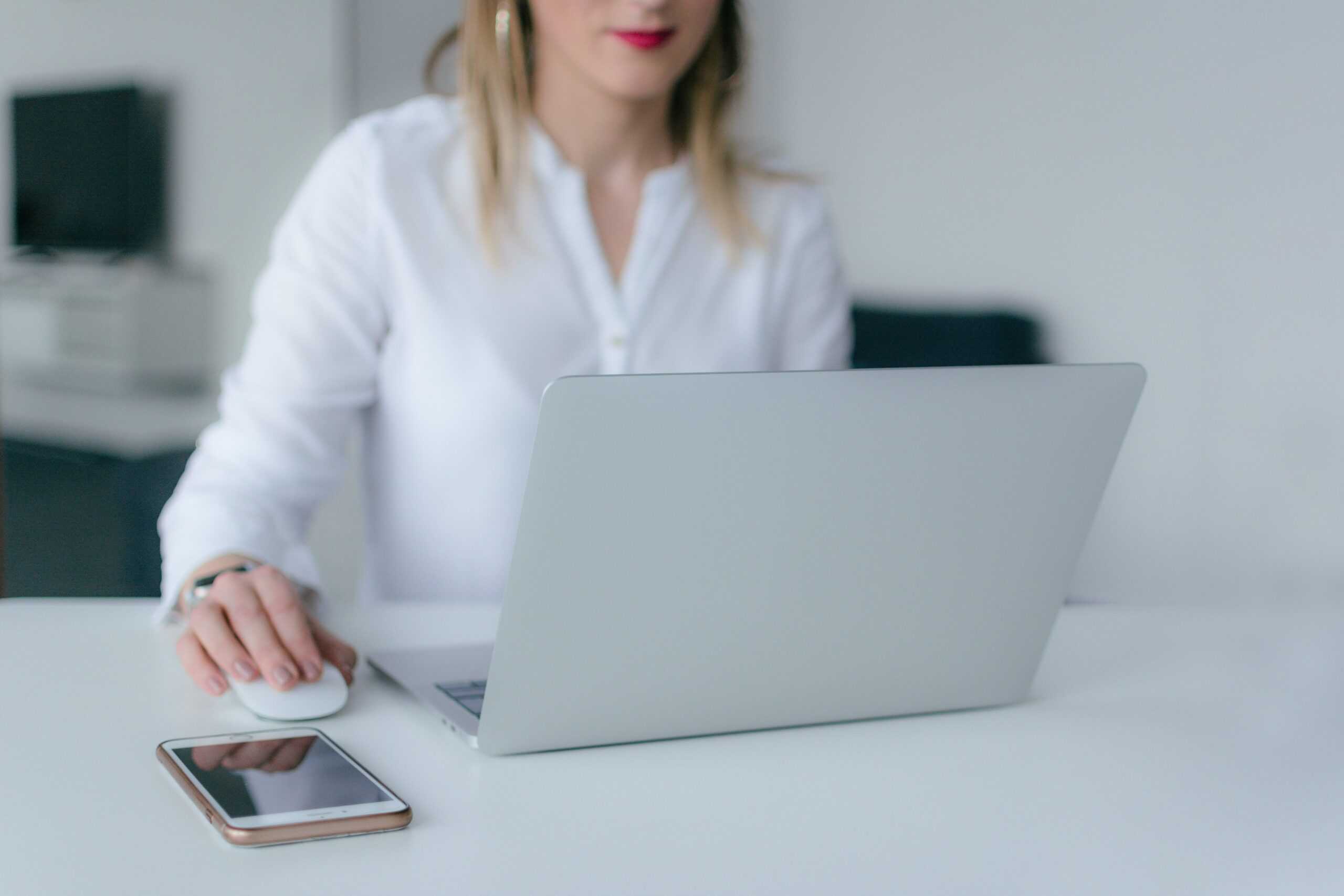 A business owner drafts a BYOD policy on her laptop with her cell phone on the table nearby.