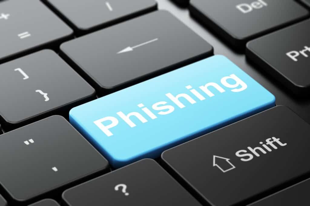 A black laptop keyboard with one blue key that says “Phishing”, a common email cyber attack.