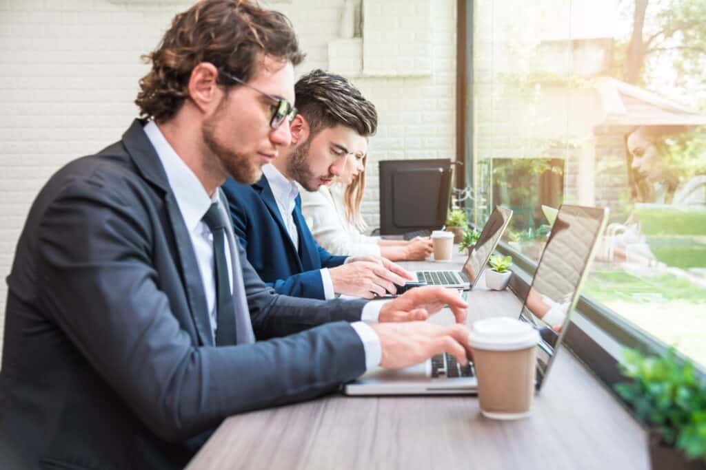 Three coworkers work on their laptops and phones, showing a need for managed IT services.