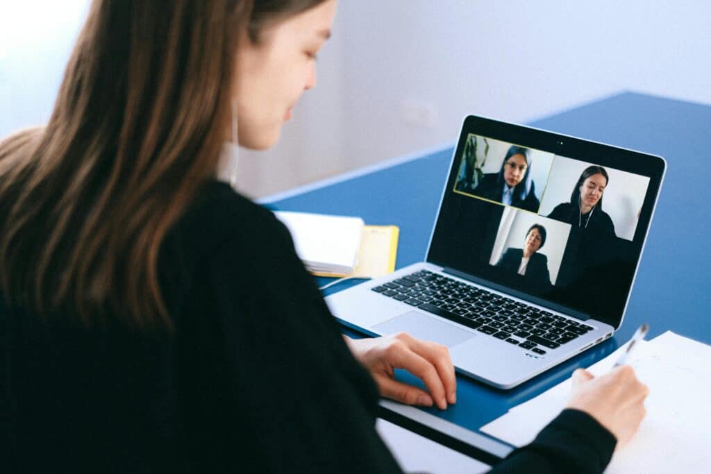 An employee has a video meeting with three other coworkers on her laptop while she writes notes.