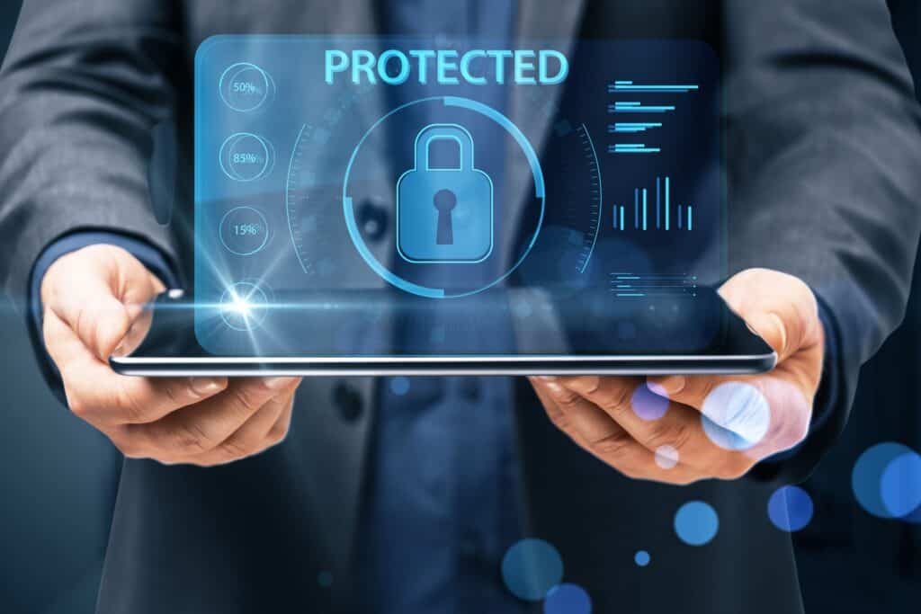 Hands hold a tablet showing a blue holographic security interface with a central padlock and the word PROTECTED.