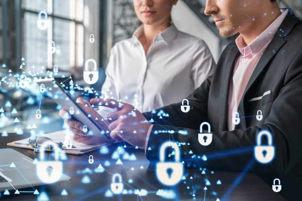 Two business owners look at a tablet as holographic blue locks in front depict cybersecurity.