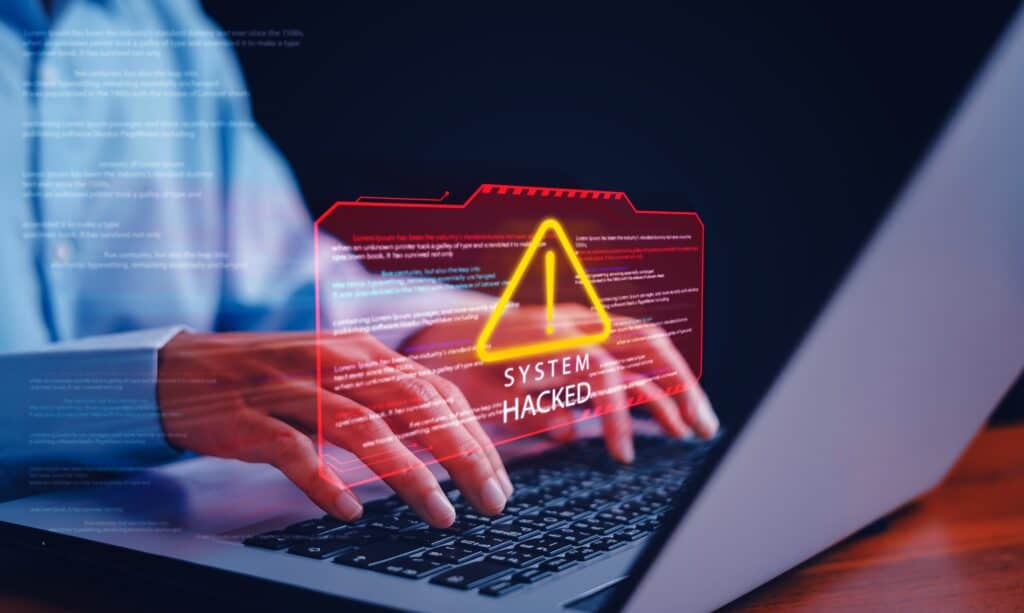 A holographic warning above a laptop screen announces that the system has been hacked.