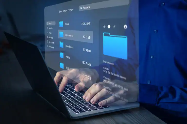 Hands typing on laptop with secure cloud storage folders visible, illustrating protected file access amid workplace distractions.