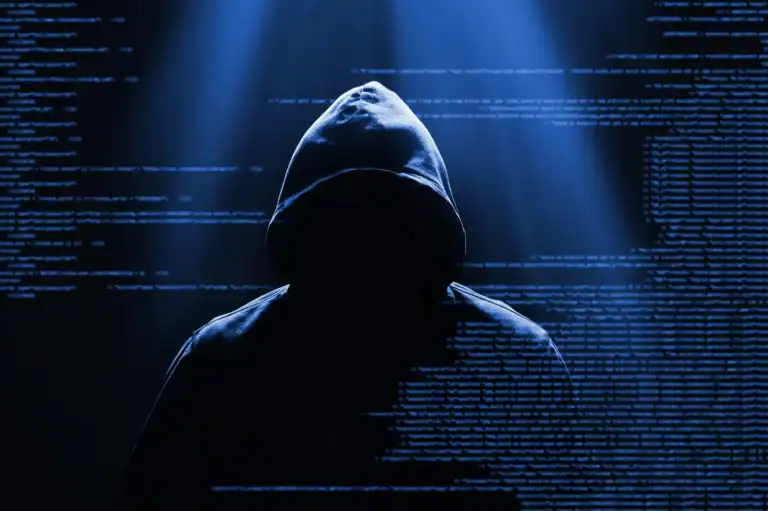 A hooded cybercriminal silhouetted against digital code, illustrating hidden cybersecurity risks for businesses.