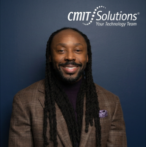 Professional headshot of Toussaint Carpenter, President & Fractional CIO at CMIT Solutions of Northwest Metro Detroit, smiling while wearing a brown blazer against a blue background with the CMIT Solutions logo.