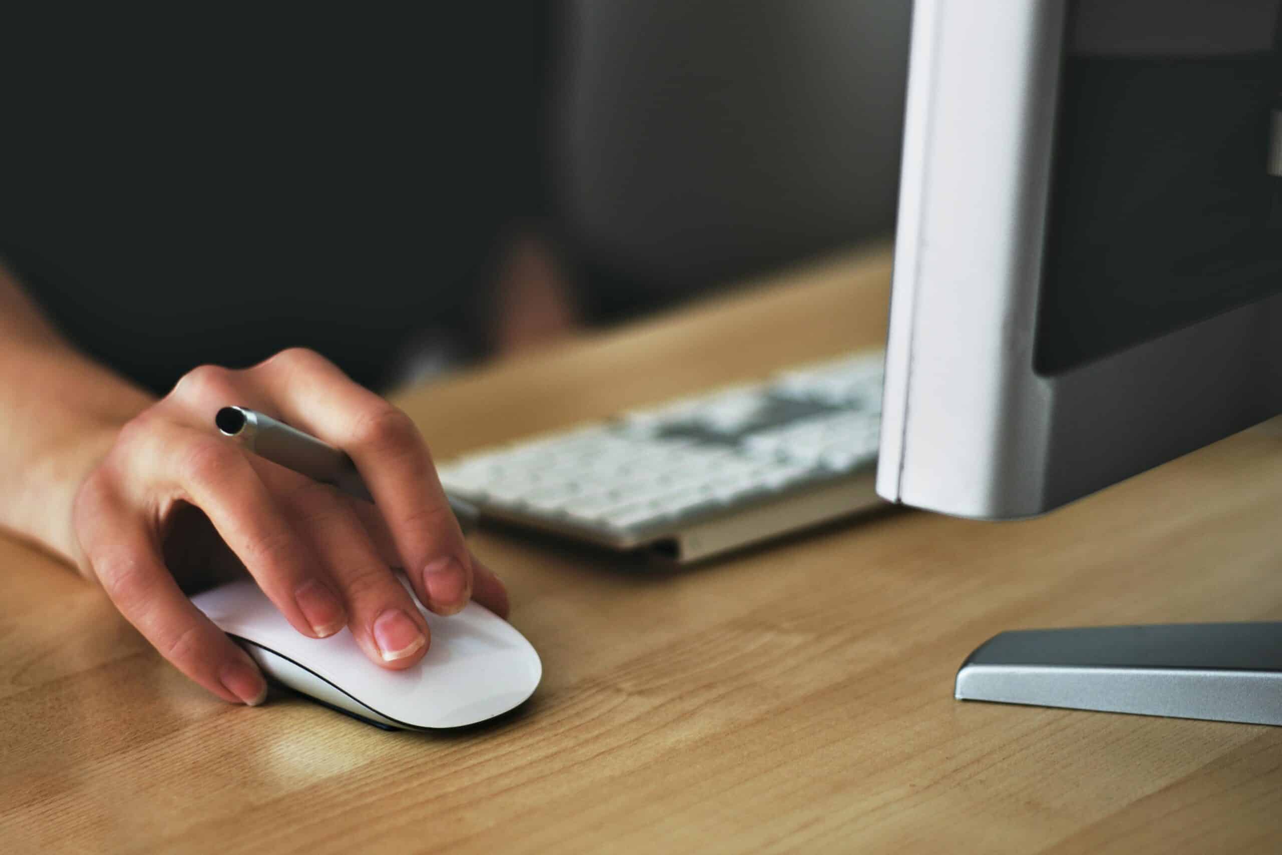 A close-up image of a hand resting on a mouse under a monitor.