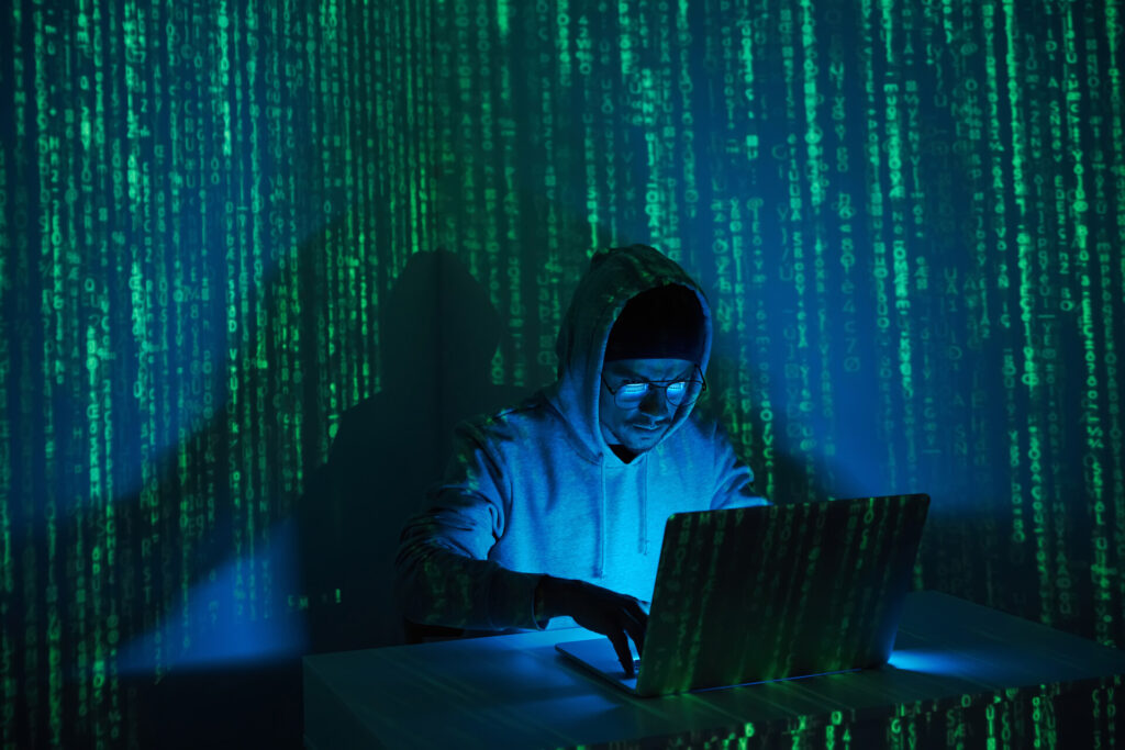 concentrated man in hooded shirt using computer in dark room
