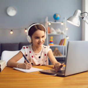 Elementary school aged girl in polka dot shirt smiling while working in online classroom