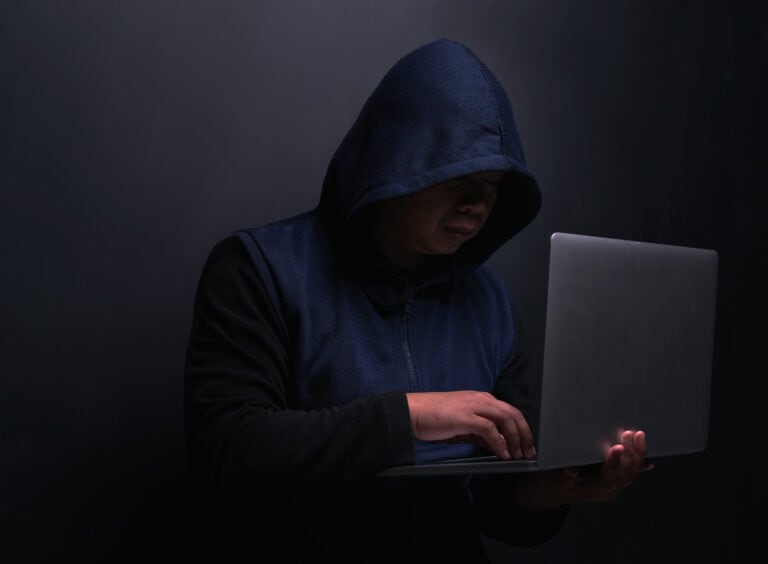 Shot of an unrecognisable hacker using a laptop against a dark background