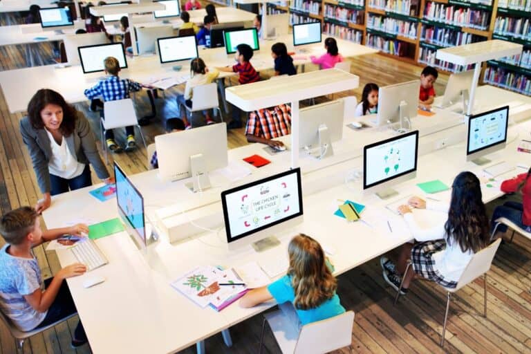 Students using computers in a classroom with a teacher assisting, highlighting the importance of cybersecurity and data protection in education.