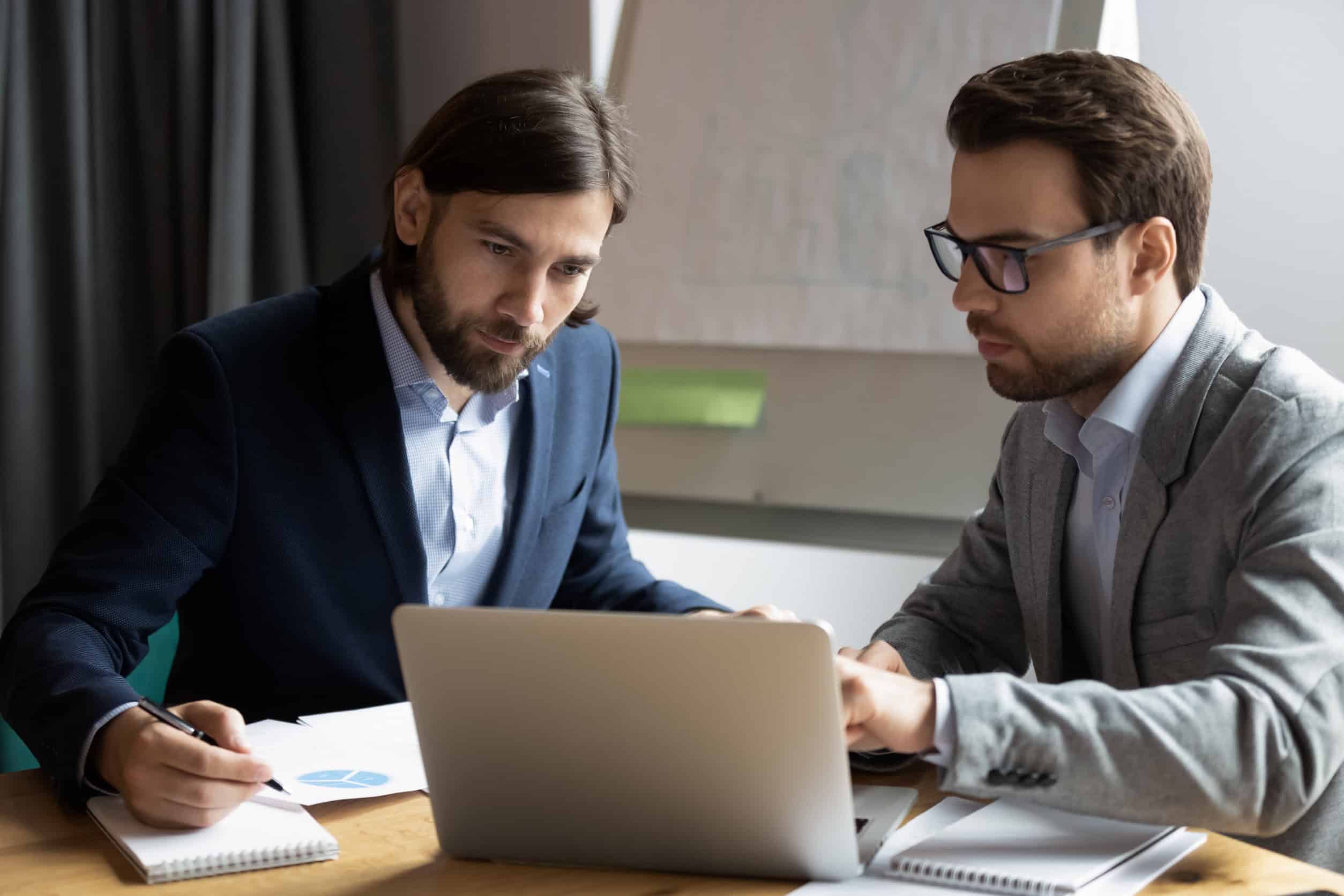 An IT specialist shows a business owner on a laptop how to make and keep his business compliant.