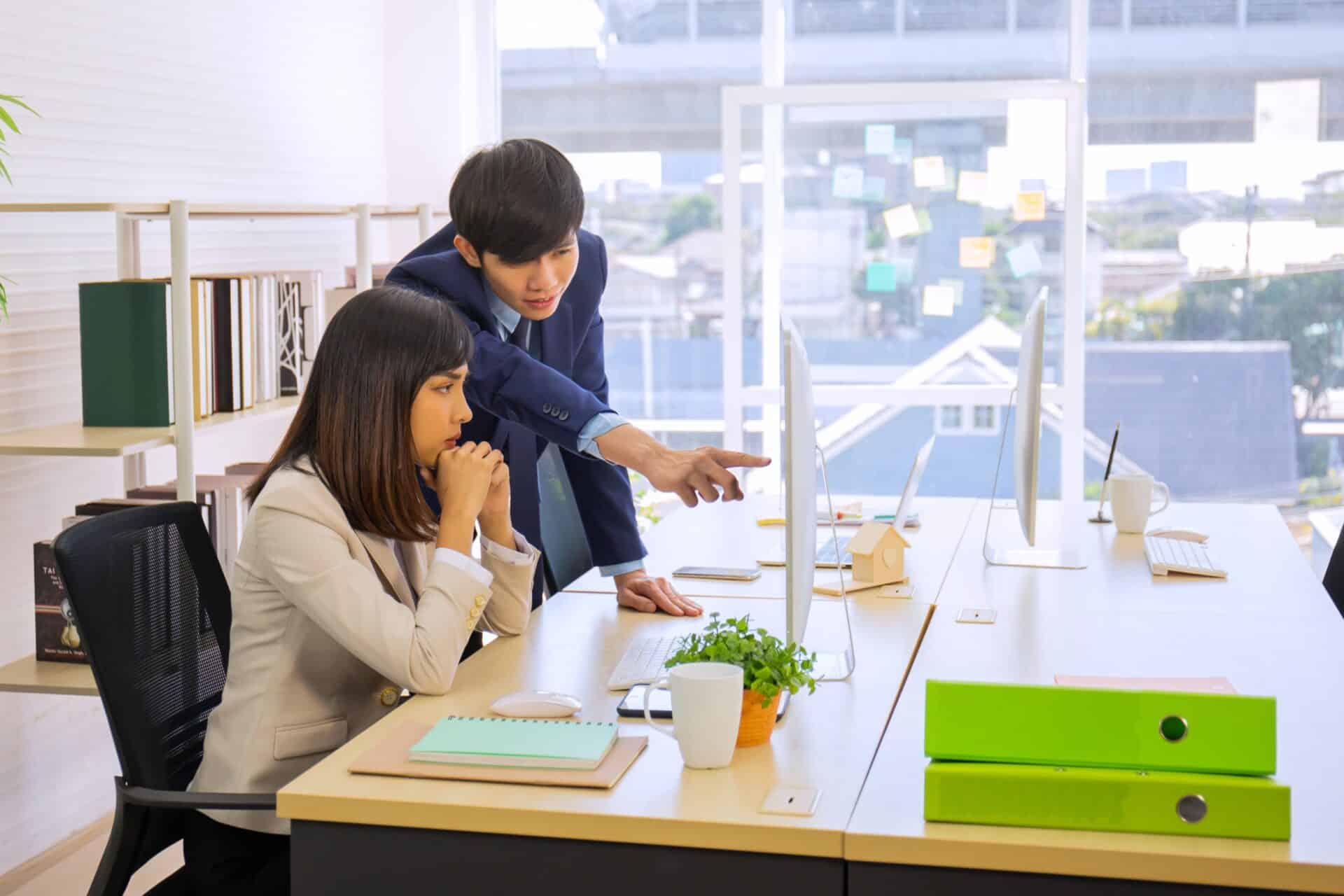 A worker points at a computer screen as a coworker looks on with interest.