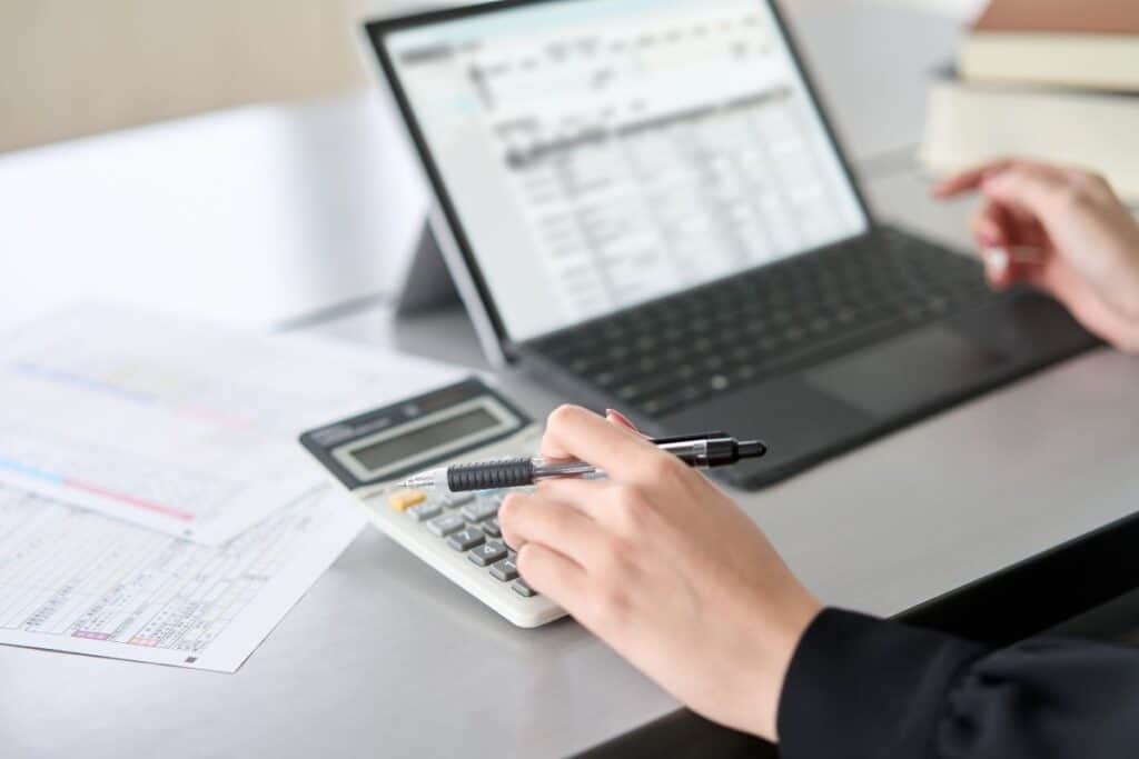Close-up of a person using a calculator and reviewing tax documents on a laptop, highlighting cybersecurity best practices for the 2025 tax season.
