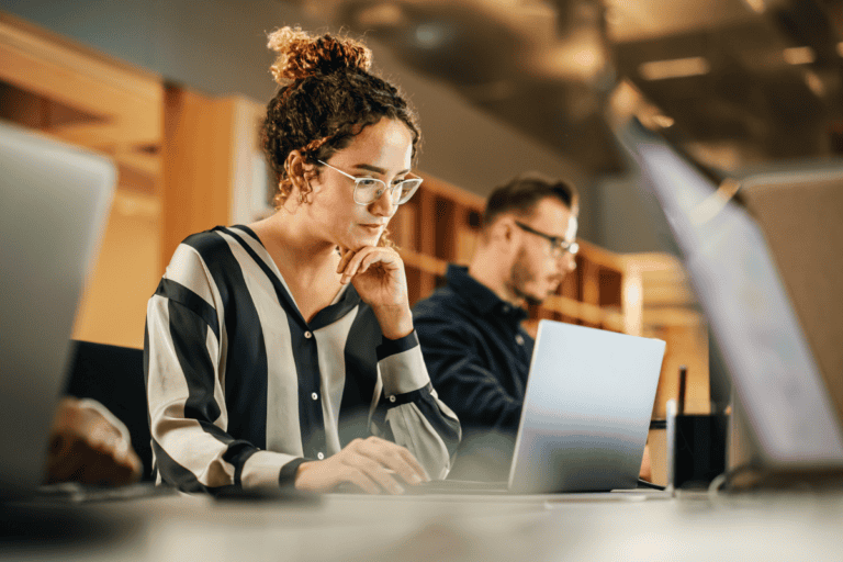 Portrait of Enthusiastic Hispanic Young Woman Working on Computer in a Modern Bright Office. Confident Human Resources Agent Smiling Happily While Collaborating Online with Colleagues.