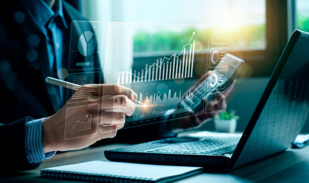 Business professional interacting with a holographic data dashboard projected over a laptop screen while taking notes.