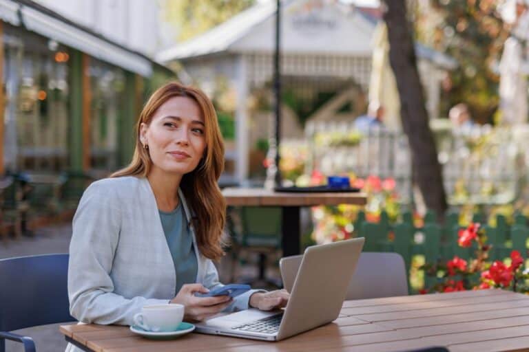 Woman at laptop in bustling cafe with drink nearby