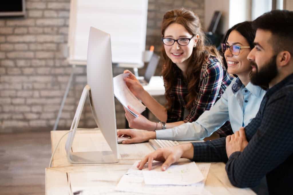 A bespectacled IT worker shows two coworkers on their monitor how to fix their current IT problem.