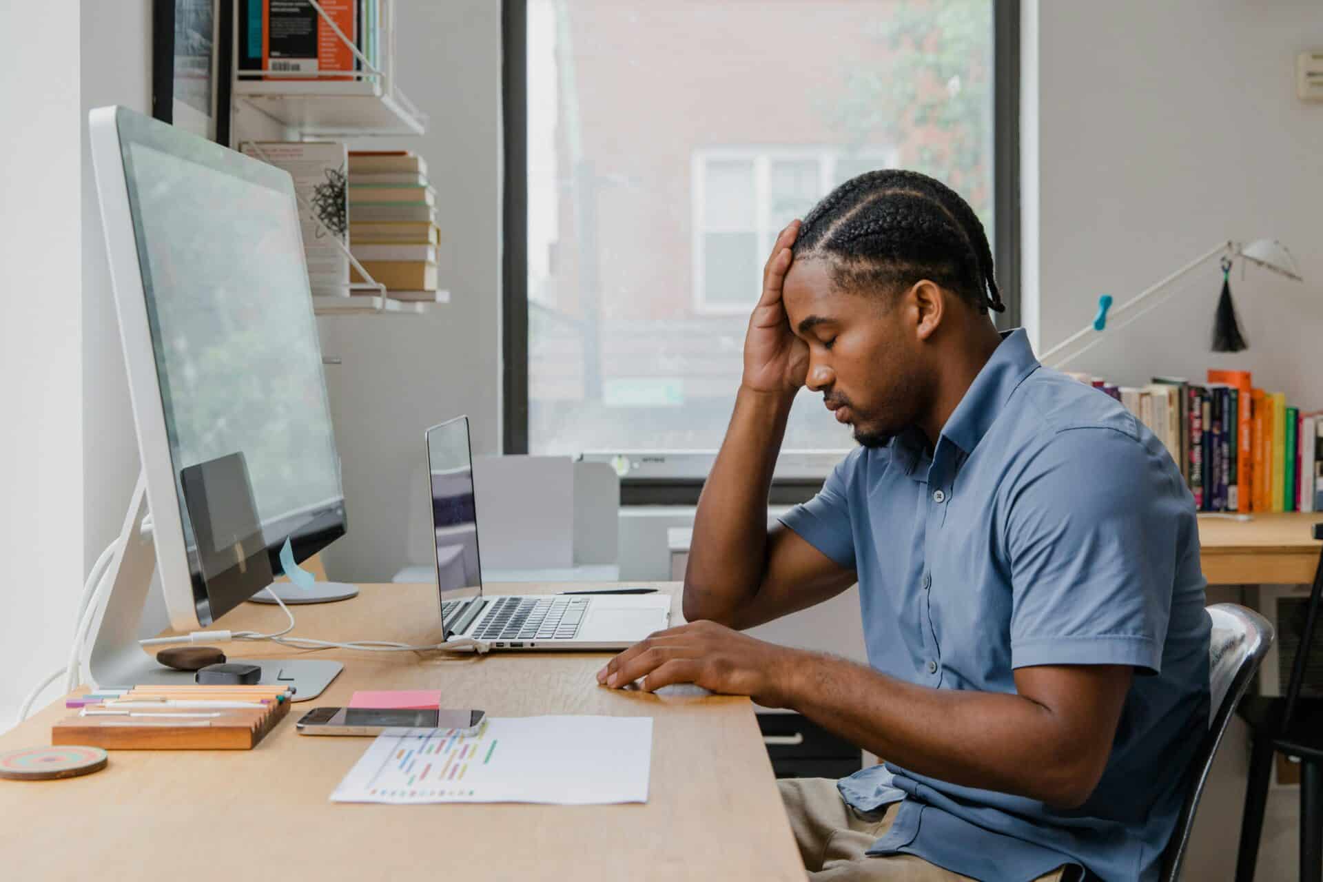 An employee puts his hand to his forehead because his desktop needs IT support.