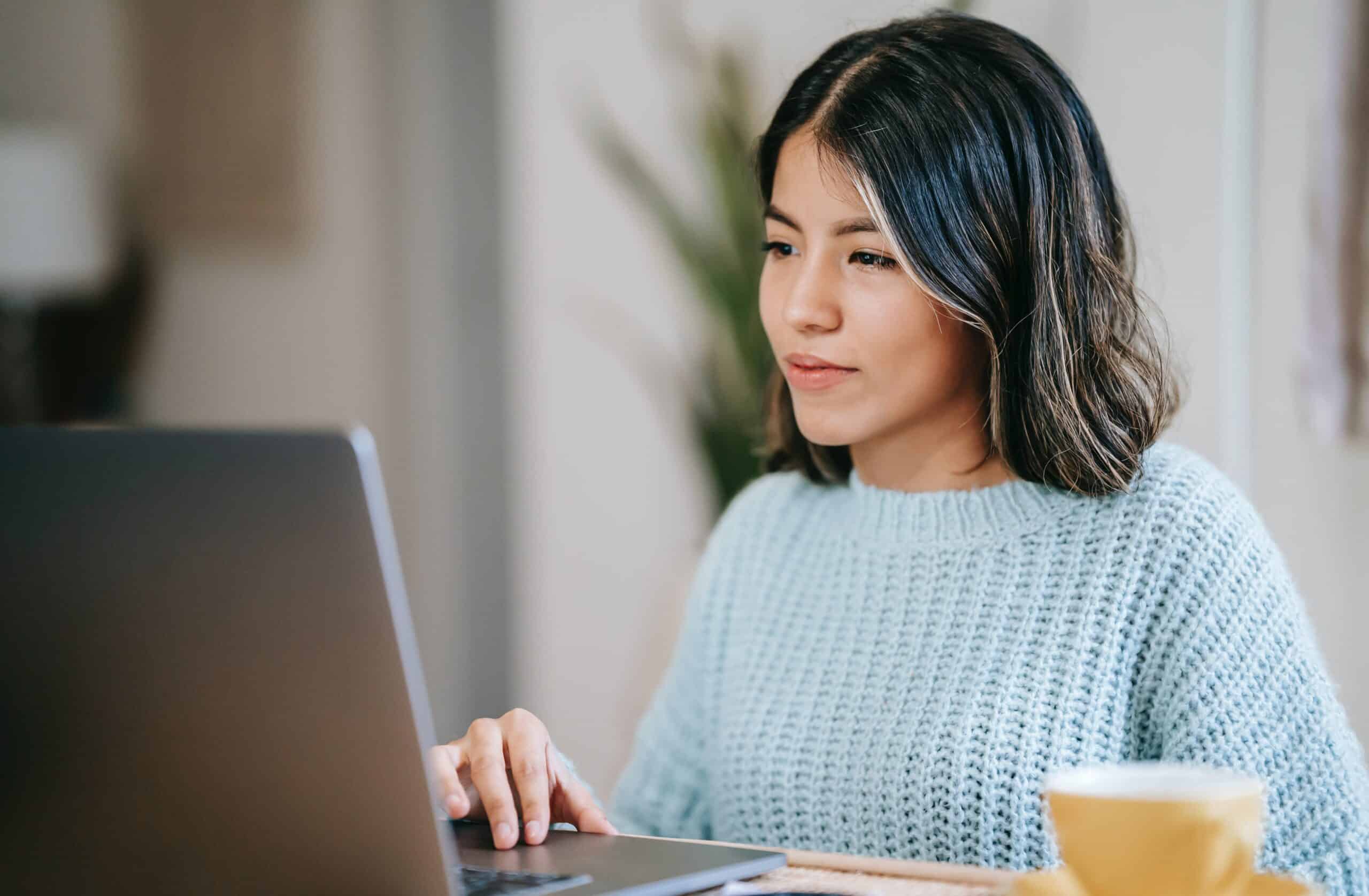 A woman on a laptop smiles at the screen as she updates passwords to protect against cyberstalking.