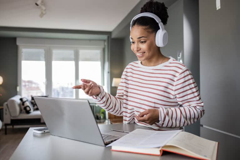 Young woman at home. She is attending an online meeting. Woman with wireless headphones is presenting ideas to her team.