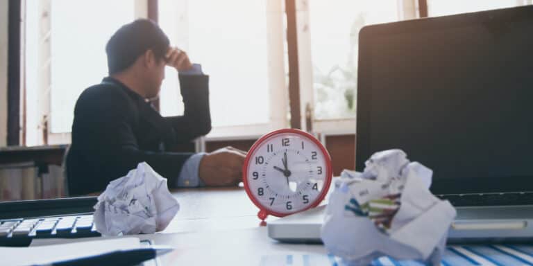 A depressed businessman sits at his desk with a computer and crumpled business reports, highlighting the hidden costs of IT shutdowns.