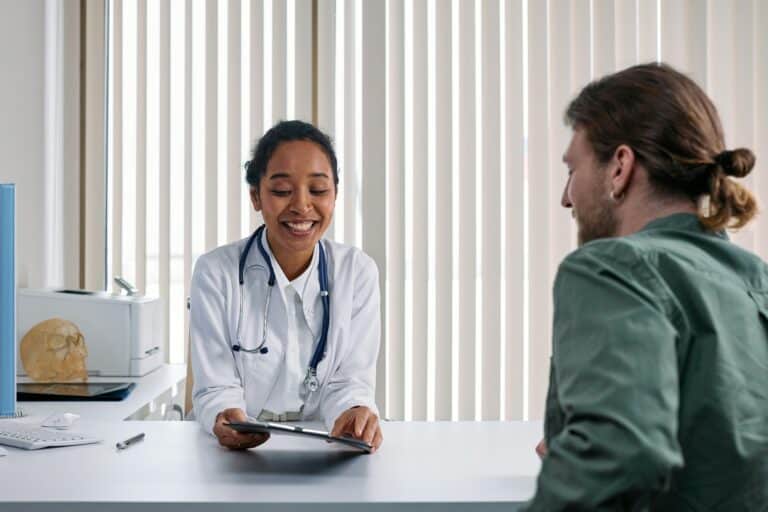 In a clinic, a doctor talks to a patient, pointing at a tablet with sensitive data.