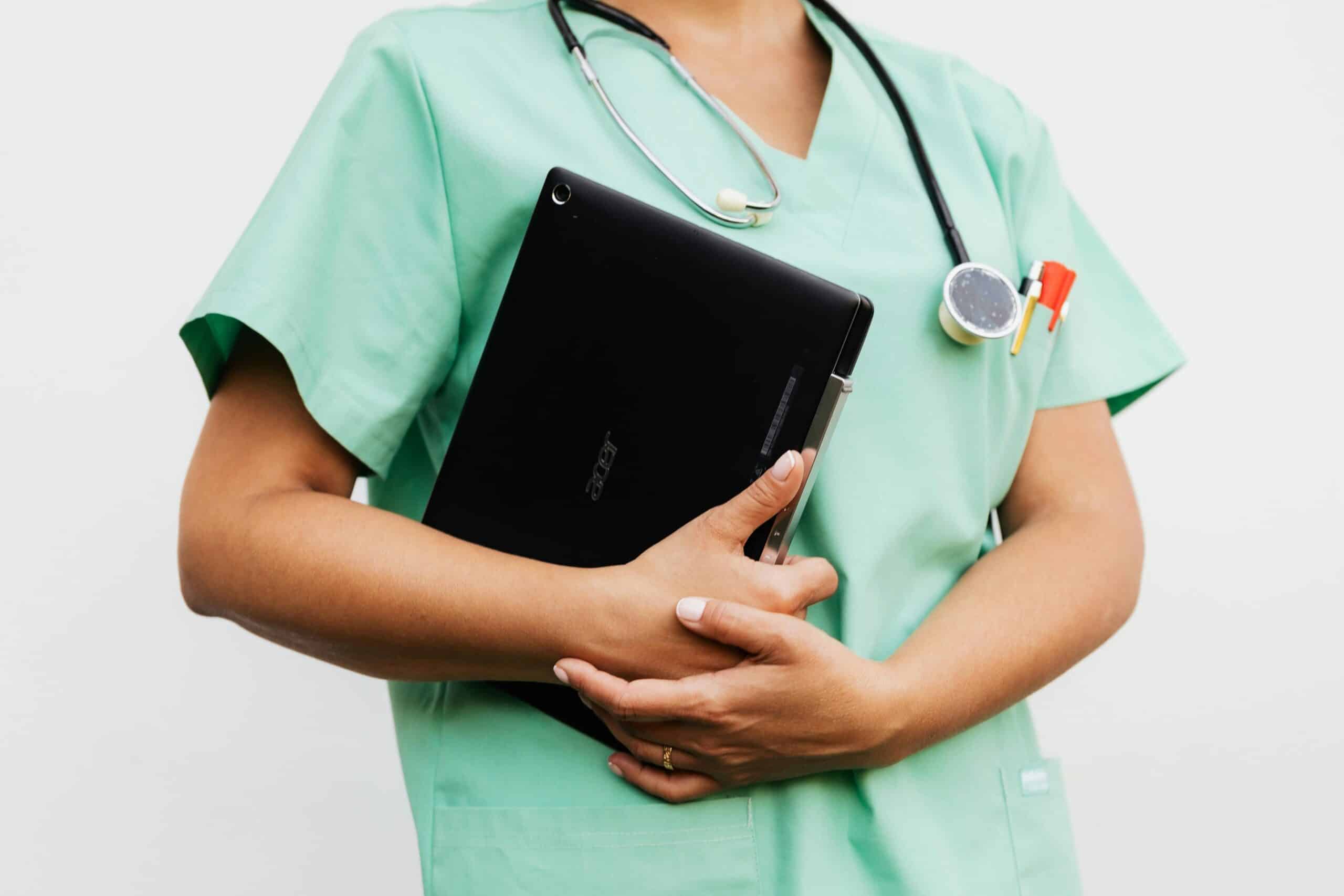 A woman in a scrub suit holding a laptop