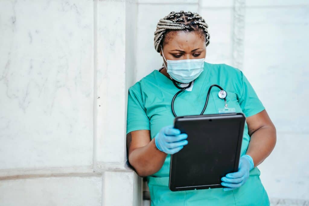 A nurse wearing a mask looks over sensitive patient data on her tablet in a clinic.