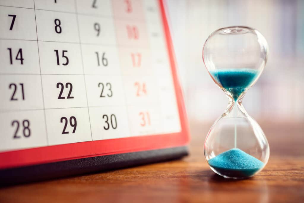 A calendar with a sand and glass hour figure next to eachother on a table. 