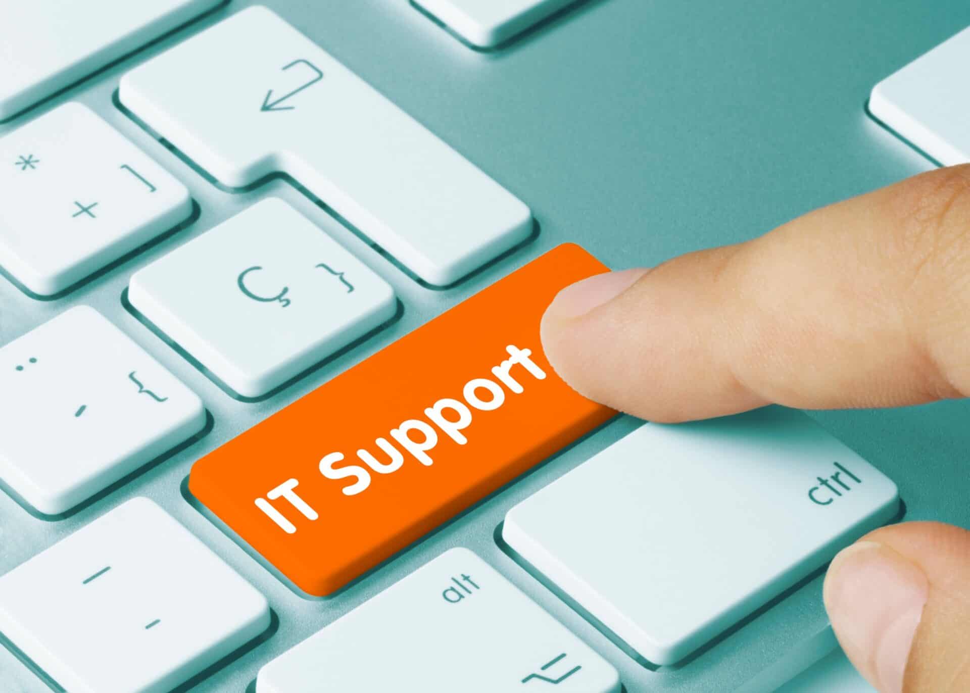 A finger presses an orange button on a white keyboard with the words “IT support” on it.