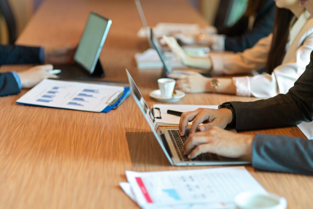 Business team collaborating on laptops during a meeting with reports and documents on a conference table.