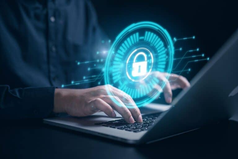 A person uses a laptop that has a blue logo with a lock depicting cybersecurity projected above.