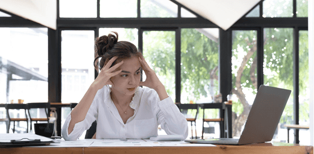 An SMB owner holds her head as she looks at her laptop, which says she needs a cybersecurity plan.