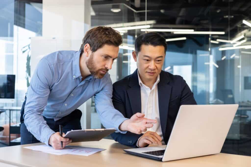 Business meeting, two business people serious concentrated discussing strategy and plans, sitting at table with documents inside office at workplace, discussing communicating looking at laptop screen