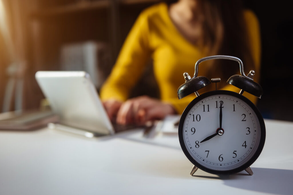 Alarm clock on the desk. Business working in modern office building or home at night using laptop.