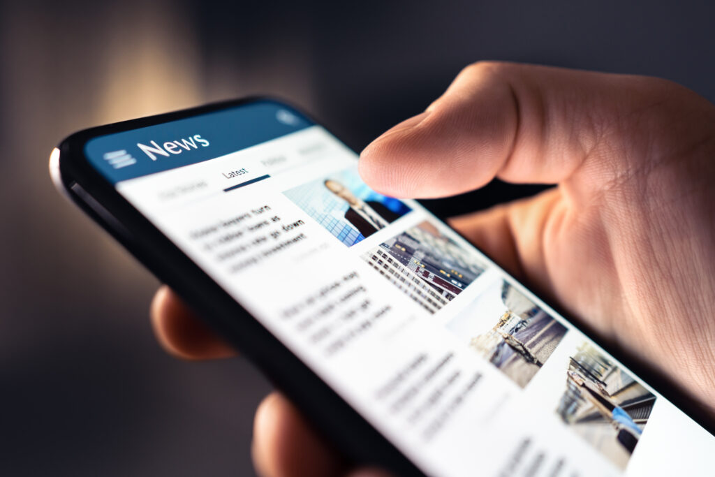Close-up of a hand holding a smartphone showing a news app with the 'Latest' tab selected and article thumbnails.