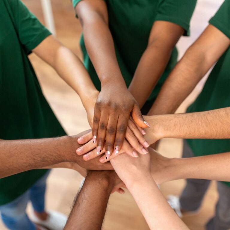 Diverse group of nonprofit volunteers stacking hands in unity, symbolizing teamwork and cybersecurity protection in education and nonprofit organizations.