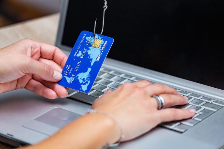 Credit card caught on phishing hook over laptop keyboard