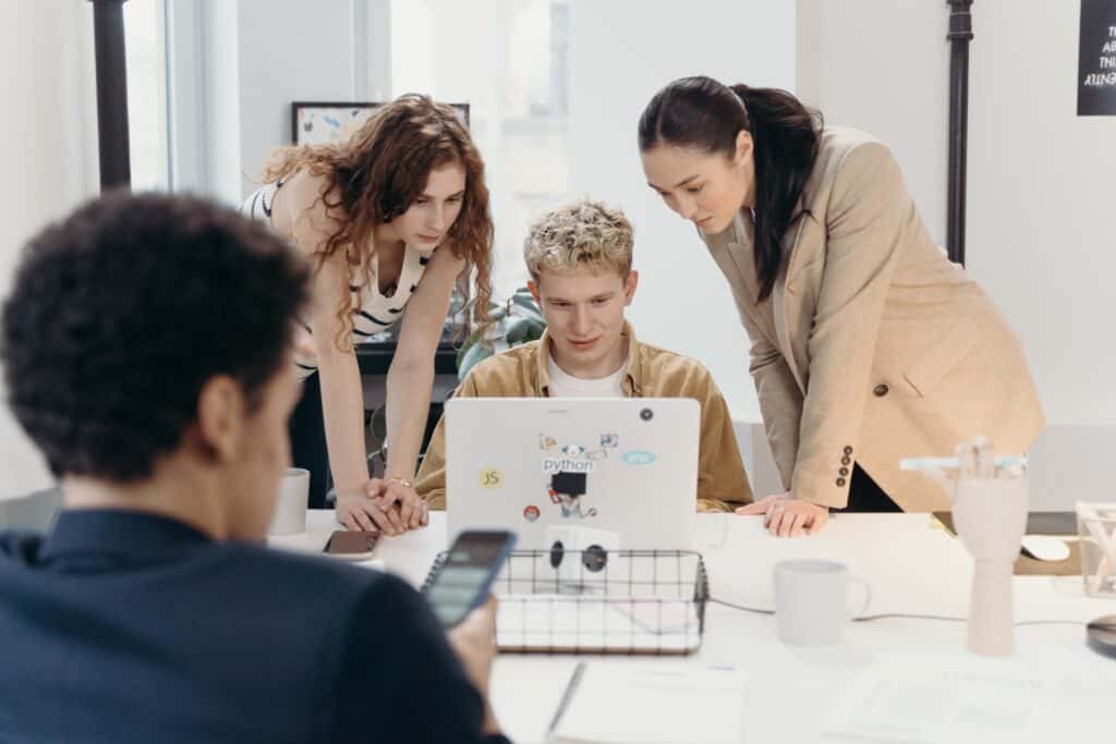 Three coworkers look worriedly at a computer as they realize their data has been lost.