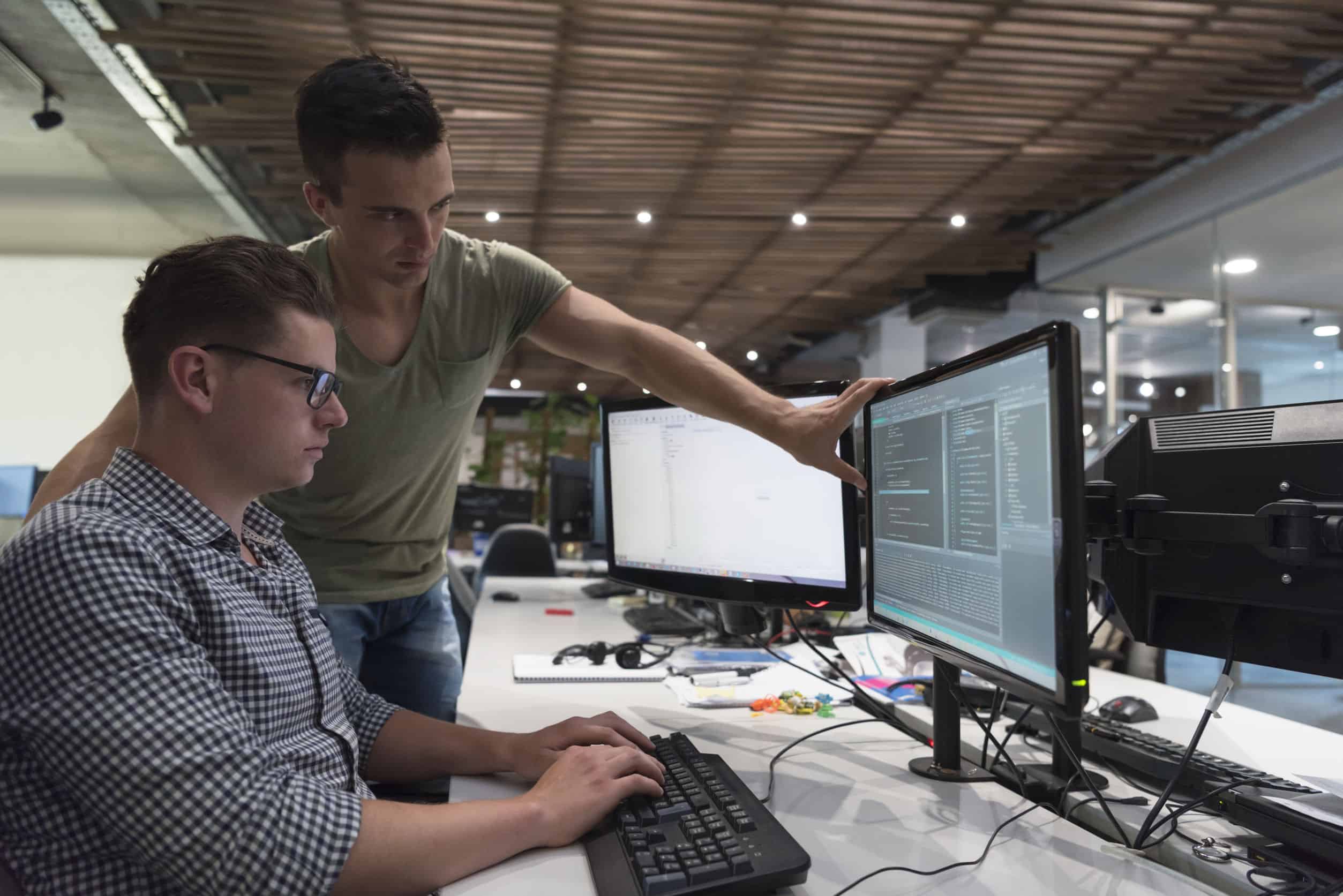 An employee points out on a coworker’s computer a cybersecurity risk that needs addressing.